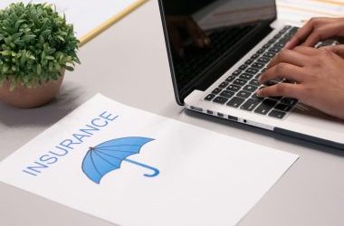 Close-up of hands typing on laptop with an insurance document visible on the desk.